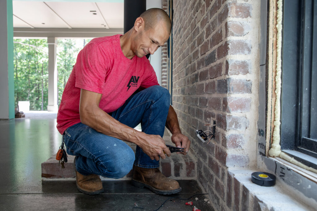 a man kneels by a brick wall, fixing an electrical outlet