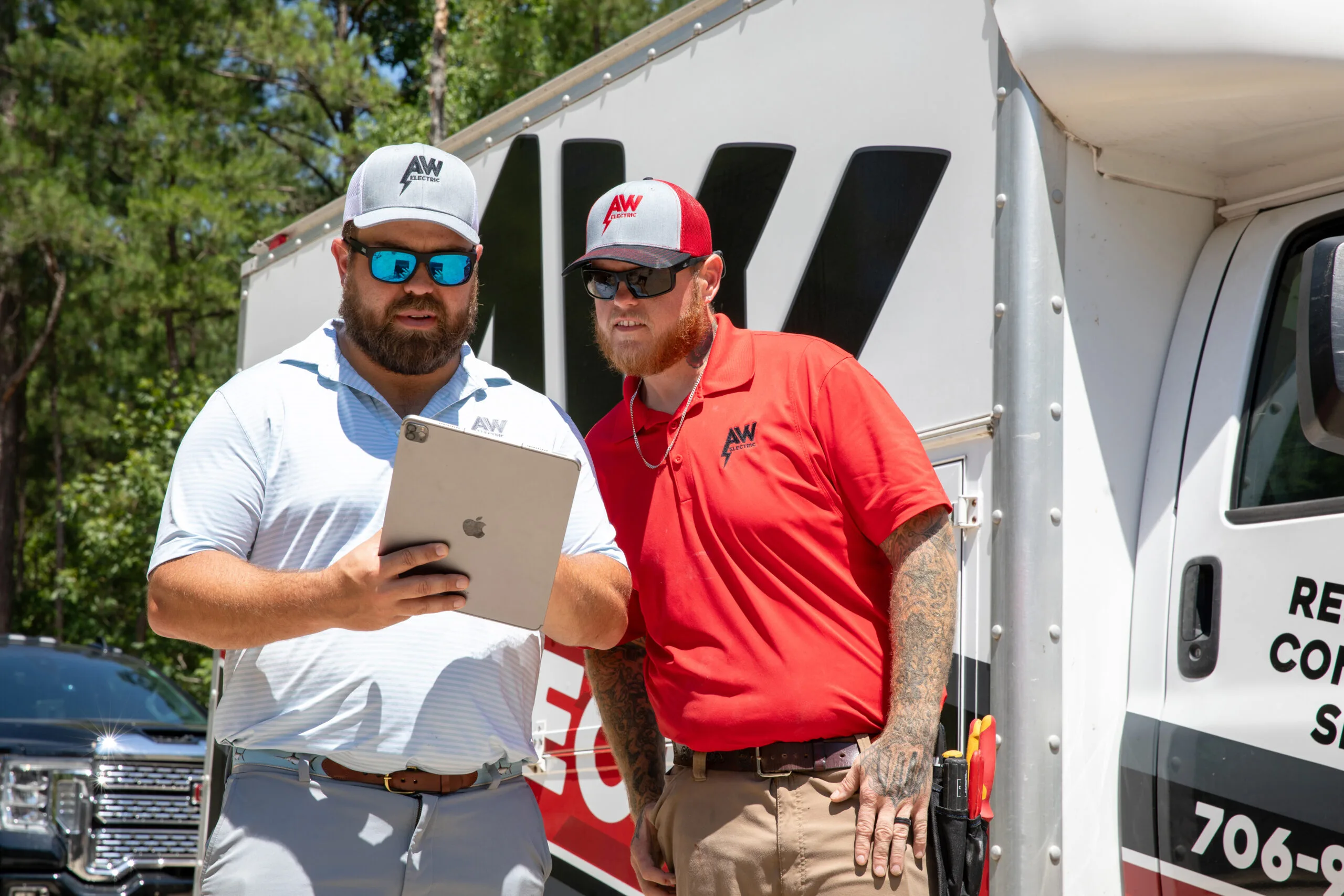 Two AW-uniformed men review an iPad beside a truck outdoors
